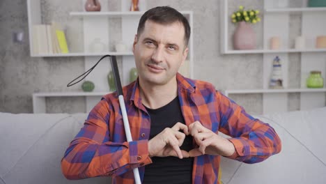 un hombre ciego feliz haciendo una señal de corazón a la cámara.