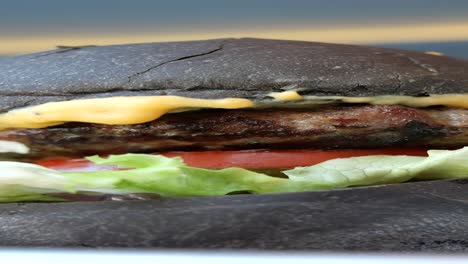 close up of a black burger with a beef patty, cheese, lettuce, and tomato