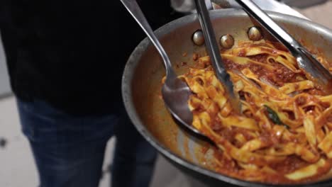 chef stirs and carries a pan filled with a pasta with meat and tomato sauce