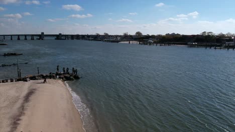 An-aerial-view-behind-people-fishing-on-a-rock-jetty-on-the-beach-in-the-East-Rockaway-Inlet-in-Queens,-NY-on-a-sunny-day