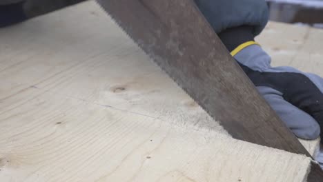 ein arbeiter mit behandschuhten händen, der das holz mit der gelben handsäge schneidet