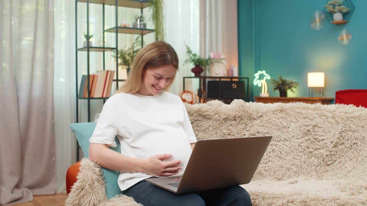 Pregnant woman lifts laptop laughs job approved message success joyful moment at home on sofa happy