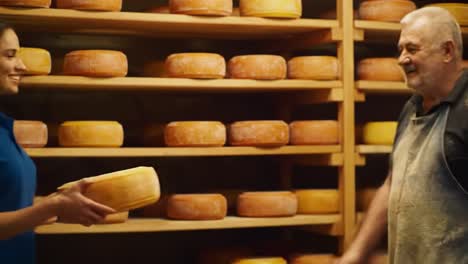a young woman and an experienced cheese maker engage warmly inside a dairy farm. they share techniques on crafting cheese while surrounded by shelves of aging wheels.