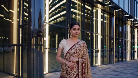 Confident Indian businesswoman in traditional sari standing proudly outside a contemporary office building, representing cultural diversity and success in the corporate world