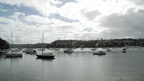 sailboats moored in bay of seaside town on partly cloudy day, wide shot