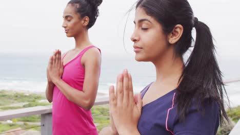 video of relaxed diverse female friends practicing yoga by sea