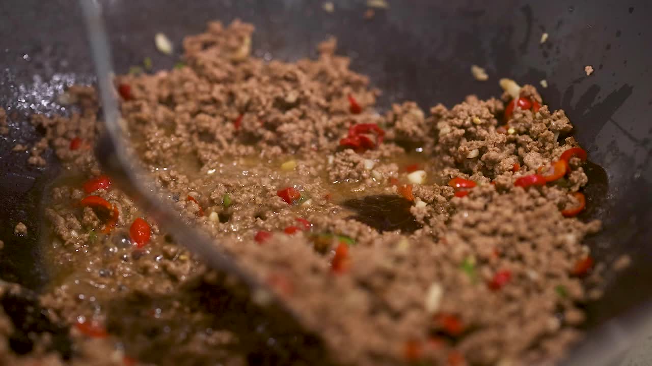 Ground beef and basil stir-fried in a wok with vibrant peppers, under warm kitchen lighting, showcasing dynamic cooking action
