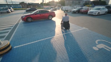 hombre con discapacidad en silla de ruedas empujando el carrito delante de sí mismo en el estacionamiento del supermercado
