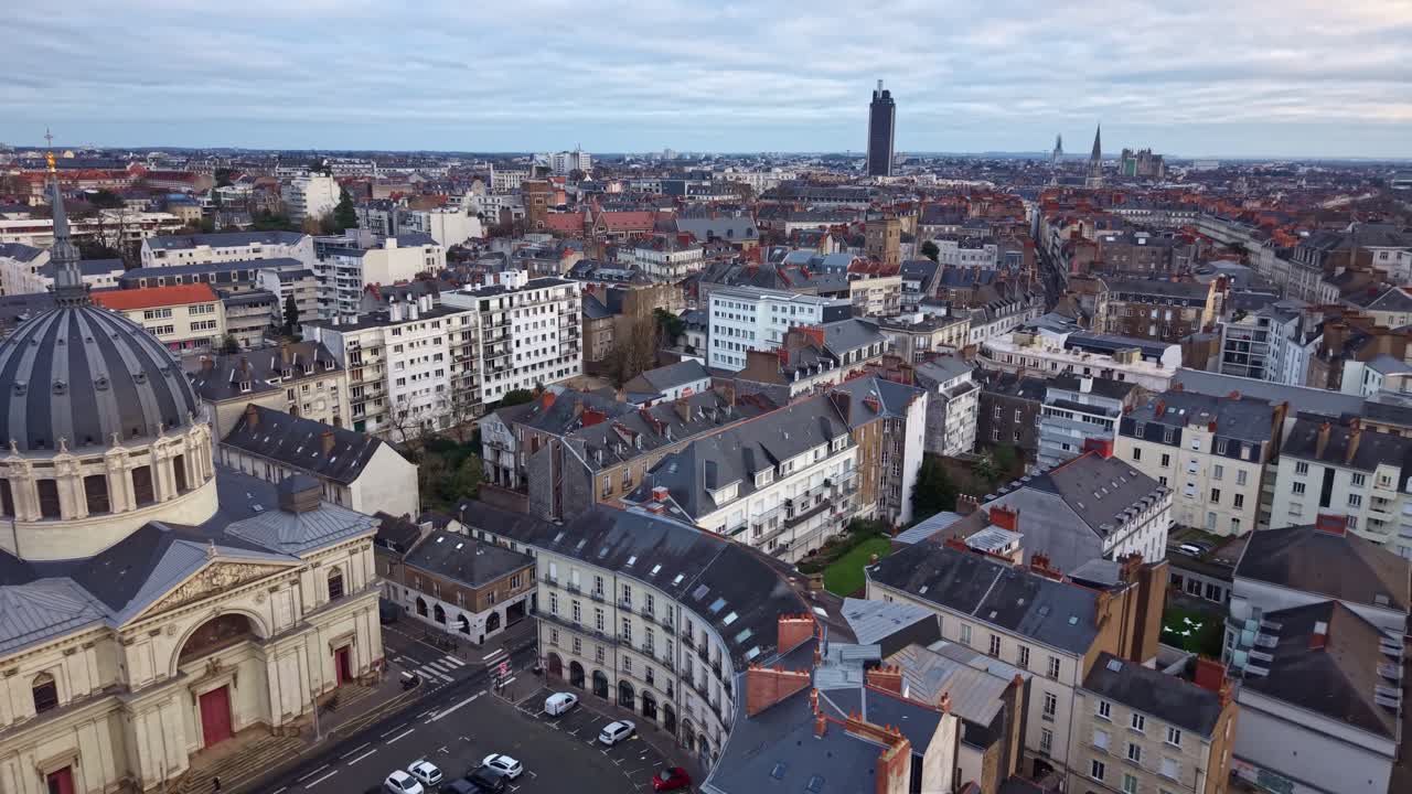 Il drone si allontana dalla cupola dell'Église Notre-Dame-de-Bon-Port rivelando il denso skyline storico di Nantes con la Tour Bretagne che si erge sullo sfondo.