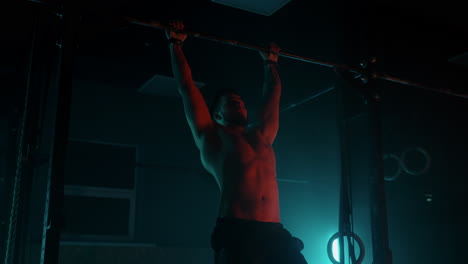 Young-man-athlete-doing-pull-up-bar-abdominal-exercise-in-gym.-Young-man-athlete-doing-pull-up-bar-abdominal-exercise-in-gym.-Slow-motion-color-light