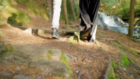 Close-up-of-couples-feet-walking-side-by-side-through-forest,-fashionable-young-couple-from-behind