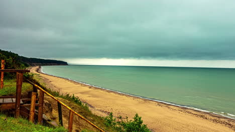 Zeitrafferaufnahme-Der-Dunklen-Wolkenbewegung-über-Dem-Meeresufer-Mit-Wellen,-Die-An-Einem-Regnerischen-Tag-Am-Sandstrand-Entlang-Krachen