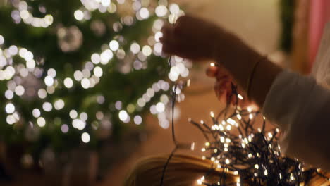 primer plano de las manos de la mujer desenredando las luces de navidad