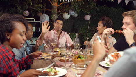 young adult friends eat and drink at an outdoor dinner party