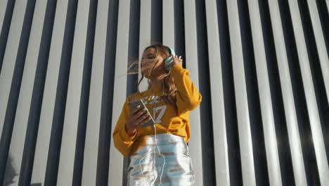 portrait of young cute attractive young girl in urban background listening to music with headphones. woman wearing yellow blouse and silver skirt