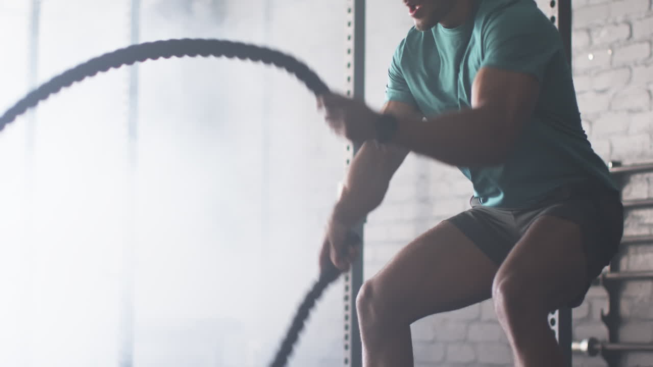Strong, fit biracial man with short curly hair and beard using battle ropes