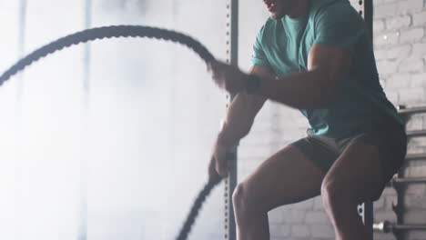 strong, fit biracial man with short curly hair and beard using battle ropes
