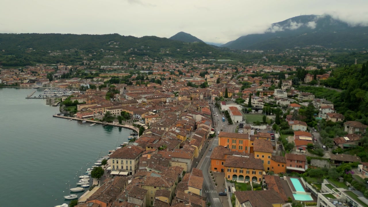 Veduta aerea che sorvola i tetti della città di Salò, la riva del lago e il porto turistico in una giornata nuvolosa