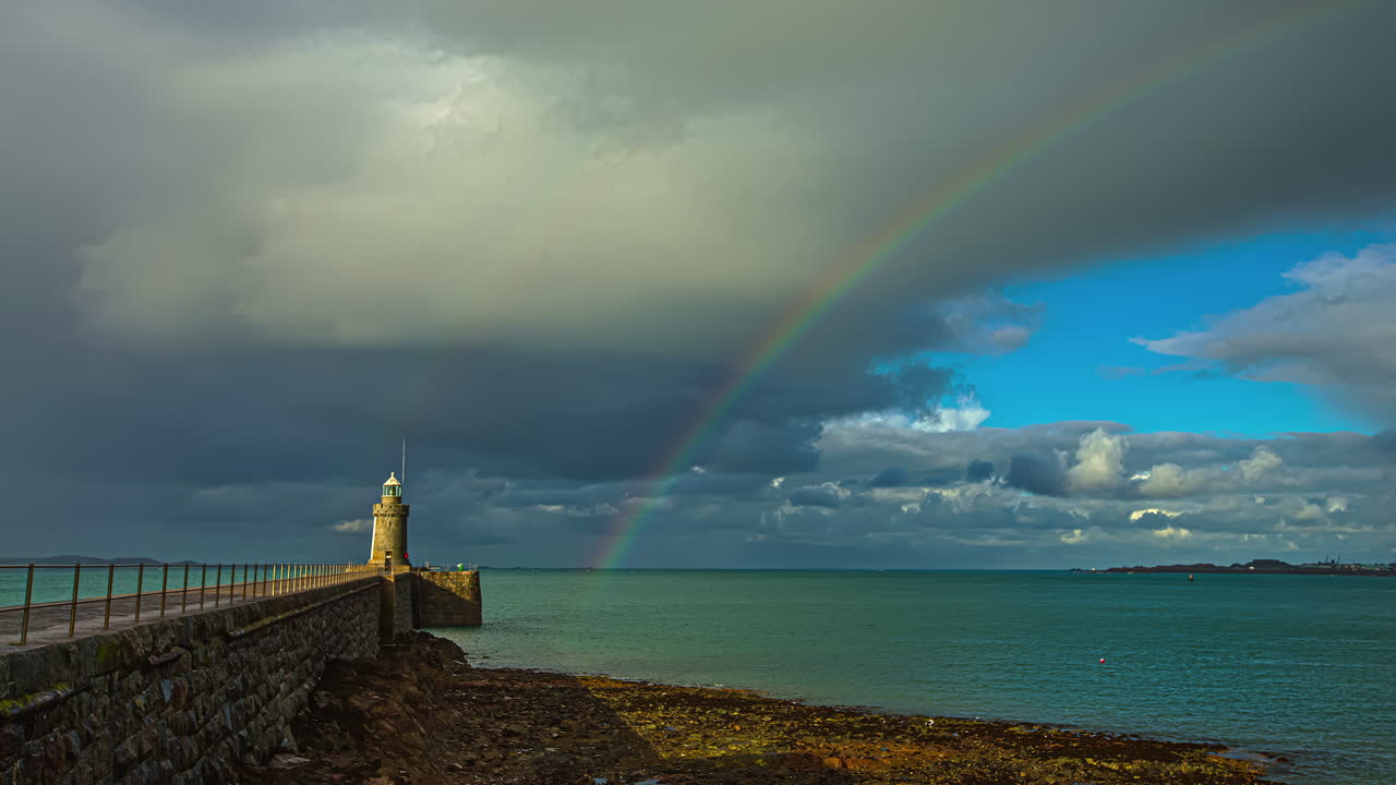 faro con vistas al mar con nubes de tormenta y arco iris en el fondo