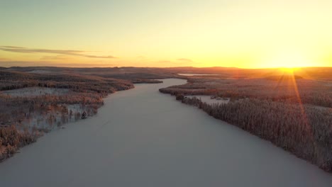 aerial view of sunset over snowy frozen lake in deep forest with hills and mountains