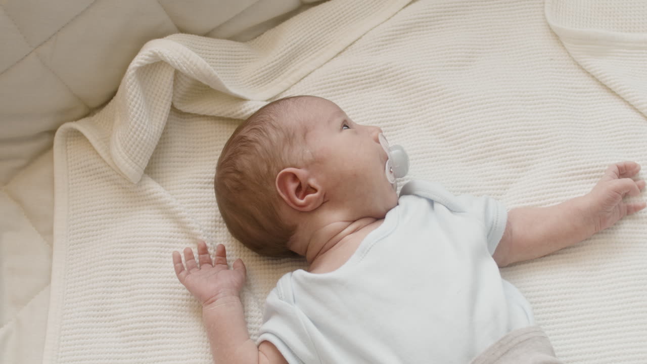 adorable bebé recién nacido acostado en la cama con un maniquí en la boca
