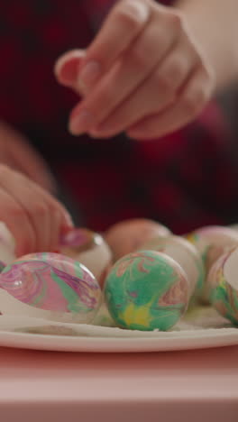 art teacher and little student put colored eggs to dry on white square plate in classroom closeup slow motion. ebru design traditions and christian holiday