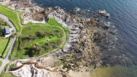 vista aérea de la playa del océano con rocas y casa costera con jardín de hierba verde