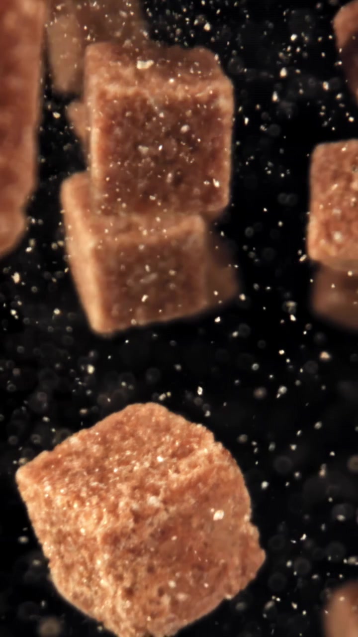 Close-up of brown sugar cubes and particles falling against black