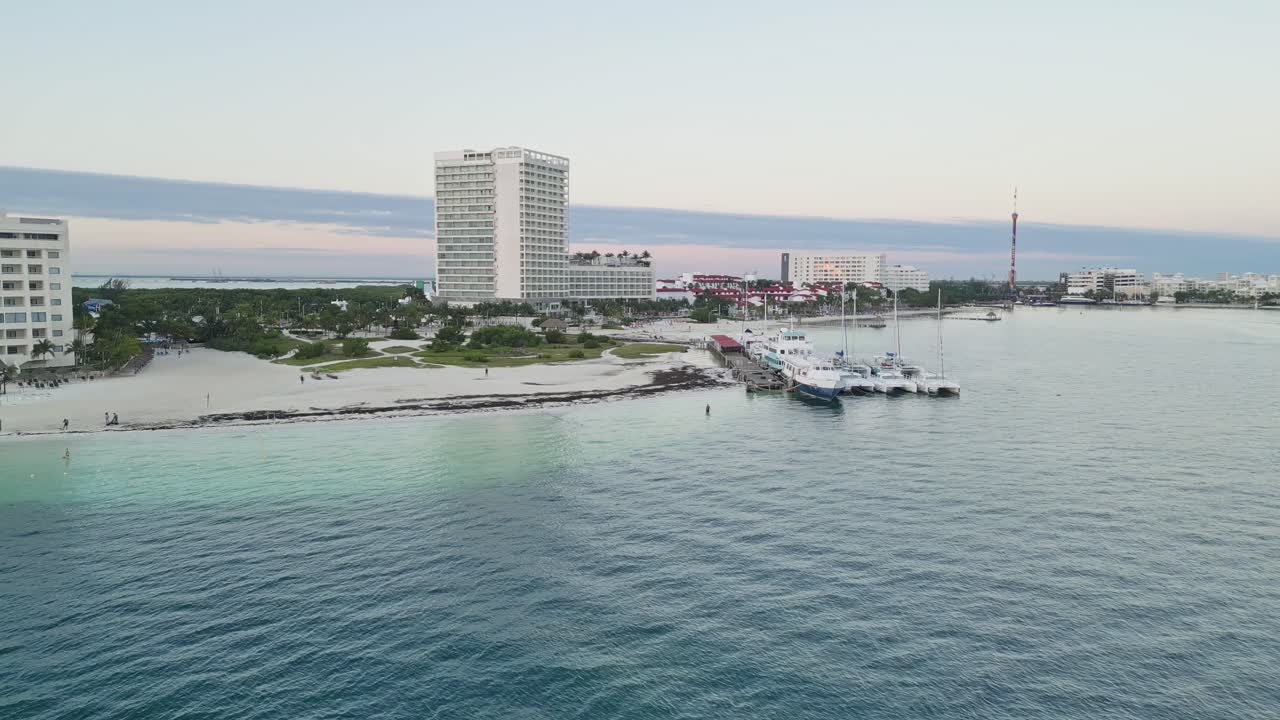 Clear view of a beach with turquoise water, hotels, and boats docked near Cancun