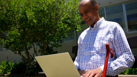 Vista-Frontal-De-Un-Anciano-Asiático-Activo-Usando-Una-Computadora-Portátil-En-El-Jardín-De-Una-Residencia-De-Ancianos-4k