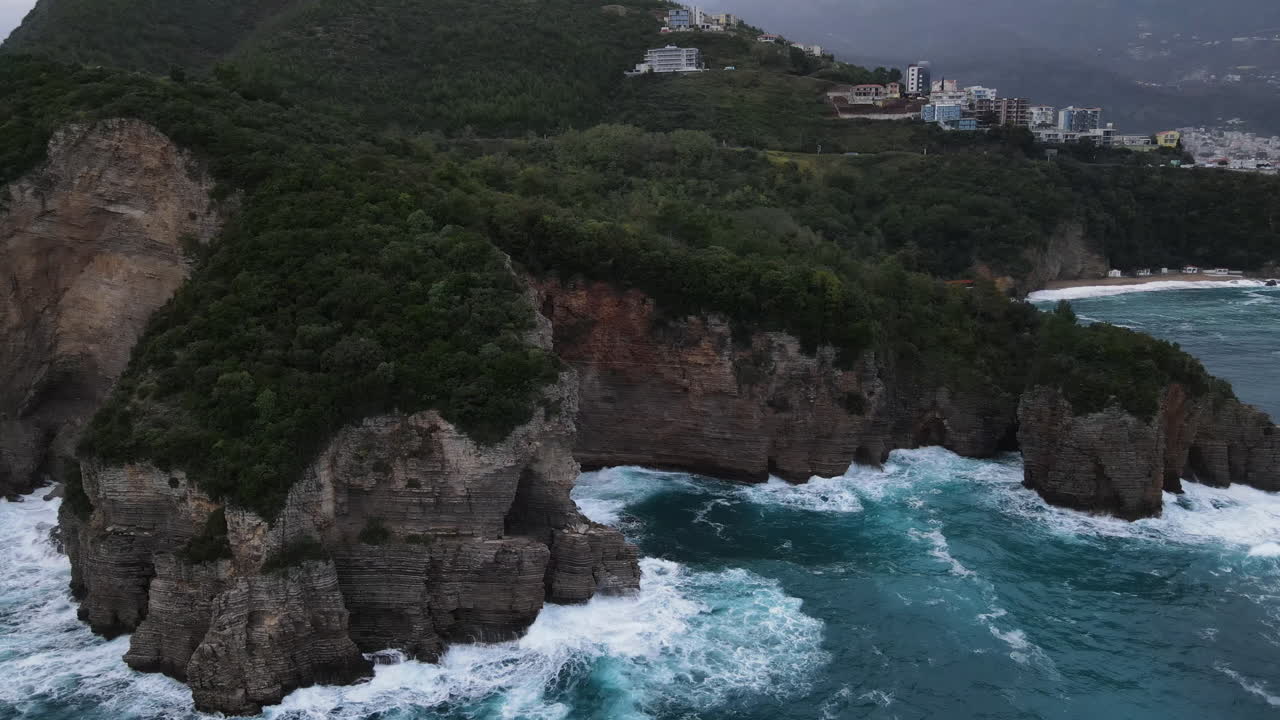 un dron aéreo disparó sobre los pintorescos acantilados y un pequeño pueblo al lado del terreno montañoso rodeado de exuberante vegetación y el mar adriático debajo en montenegro