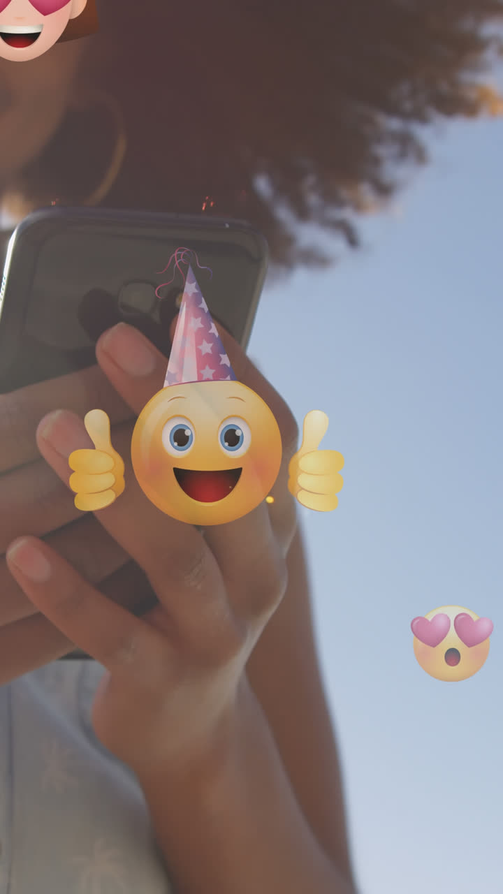 animación de emoticones sobre la sección media de una mujer biracial que usa un teléfono inteligente al aire libre