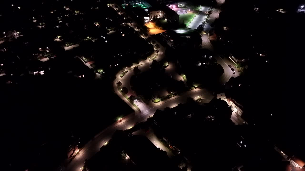 Driving car on illuminated tree-lined street at night. American suburb neighborhood from above. Peaceful and quiet city with warm glowing lanterns. Aerial top down flyover