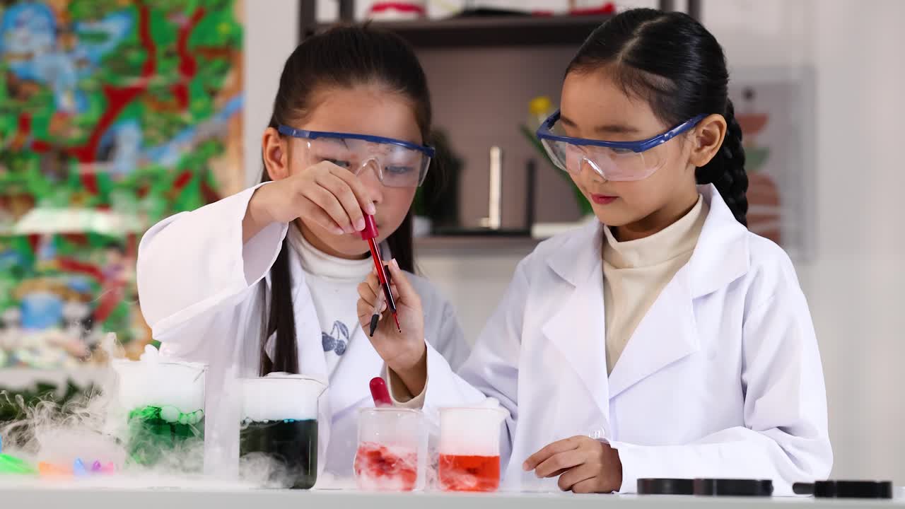To unge piger i kitler bruger pipetter til et farverigt kemieksperiment i skolen