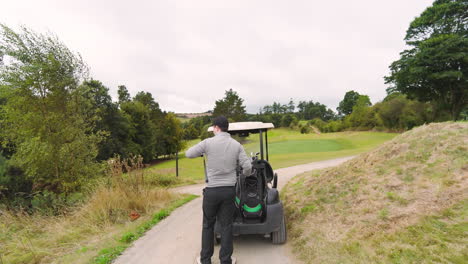 male golf player playing golf, taking club and balls from golf cart and going on a golf course