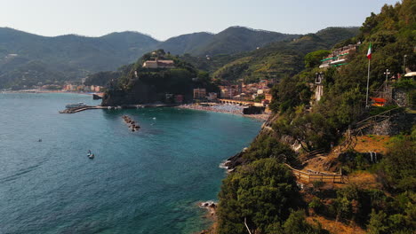 Luftaufnahme-Der-Klippe-Mit-Viel-Grün-Und-Kleinem-Haus-Und-Resort,-Umgeben-Von-Meer-Mit-Yachten,-Die-Tagsüber-In-Ruhigem-Und-Stillem-Wasser-Im-Dorf-Portovenere-In-Italien-Segeln