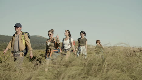 tracking shot of a happy with backpacks walking along hiking trail in row and talking