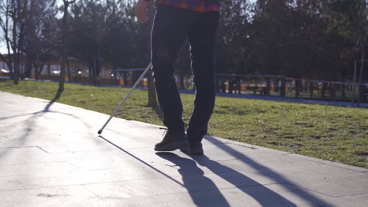Close-up of blind man's feet and cane walking on a path among trees.