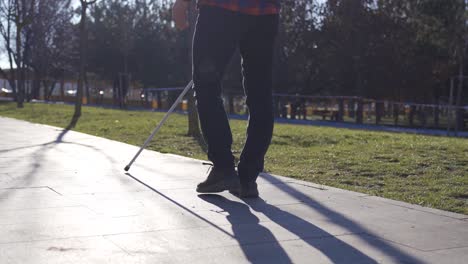 Close-up-of-blind-man's-feet-and-cane-walking-on-a-path-among-trees.