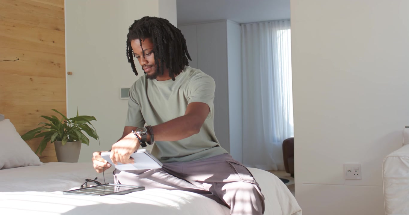 Uomo afroamericano che si rimbocca la manica sul letto, collegando un cavo, piegando un supporto e posizionando un tablet per la visualizzazione.