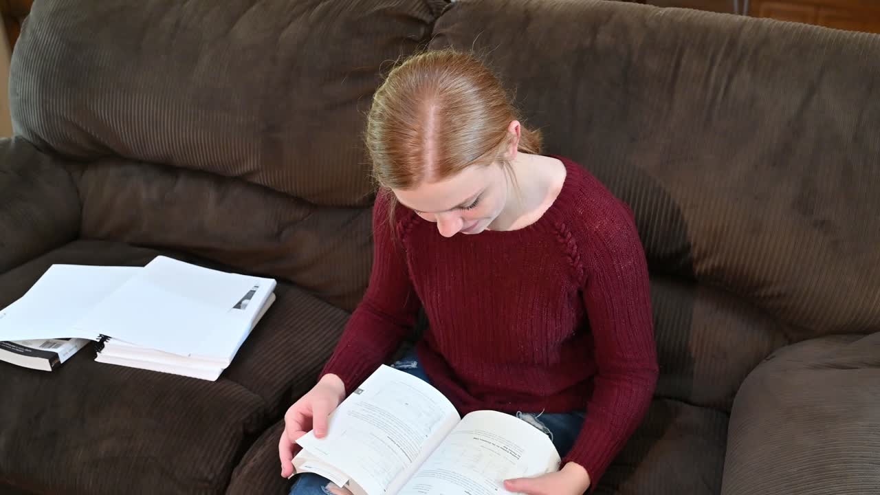 High school student, Madelyn, studies from a textbook, looks up at the camera with a huge smile
