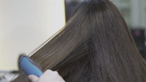 a stylist brushes and straightens a woman’s brown hair at a salon, focusing on smooth styling.