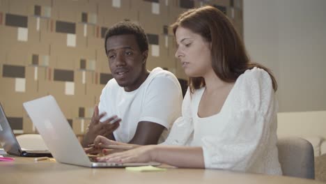 diverse couple of professionals sitting at table with laptops