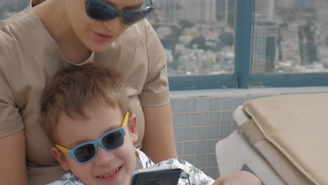 Kid-with-mother-relaxing-outdoor-and-using-cellphone