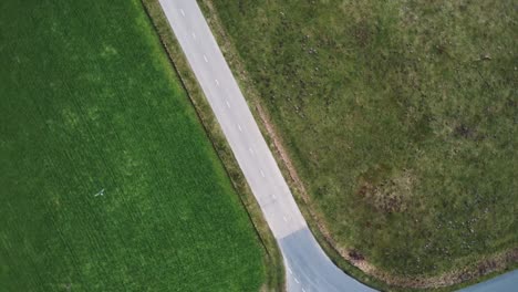 Luftdrohnenaufnahme,-Die-Sich-Mit-Einem-Motorradfahrer-Langsam-Auf-Die-Straße-Zwischen-Grasfeldern-Zubewegt