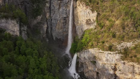 Aerial-view-of-Seerenbach-Falls,-cascading-down-a-steep-cliff-surrounded-by-lush-green-forest-in-Amden,-Betlis,-near-Walensee,-Switzerland