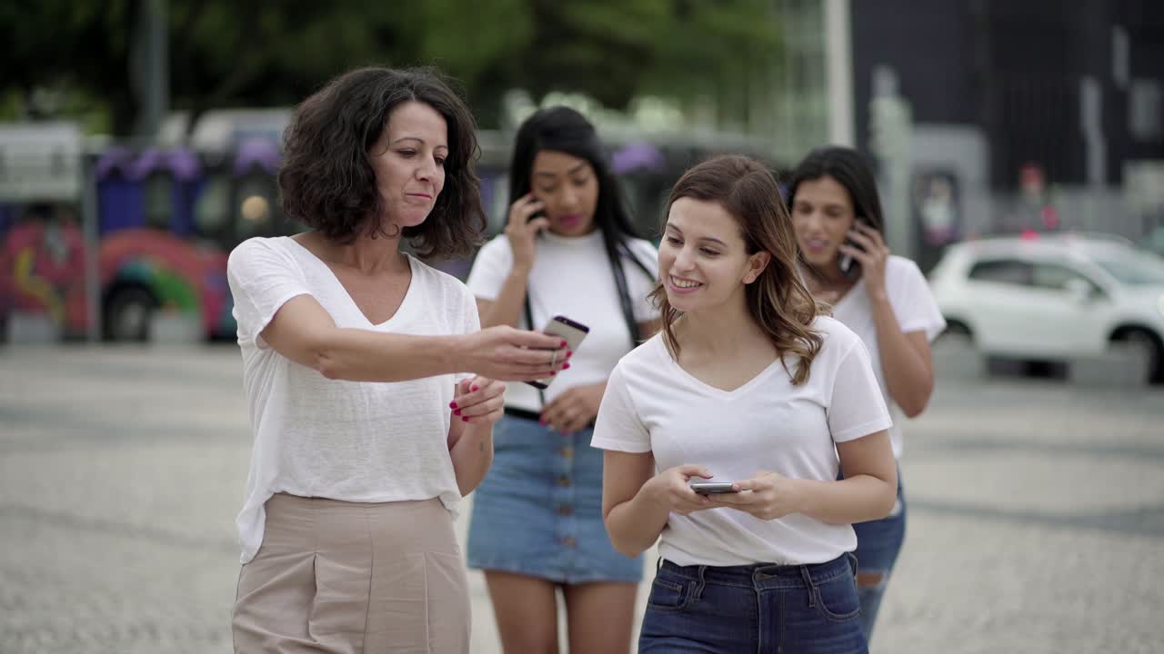 mujeres sonrientes hablando y sosteniendo teléfonos durante el paseo