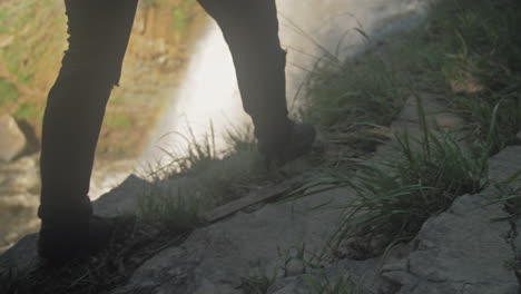 slow motion of a person walking along the ledge next to a waterfall