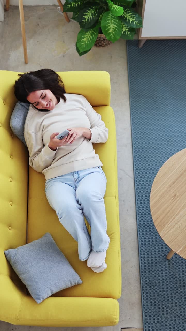 Giovane donna che si rilassa su un divano giallo e usa lo smartphone