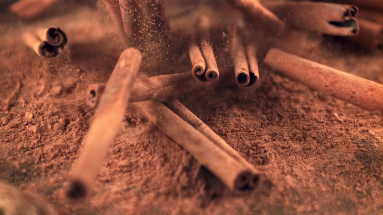 Paus de Canela Caindo sobre uma Cama de Canela em Pó em Câmera Lenta